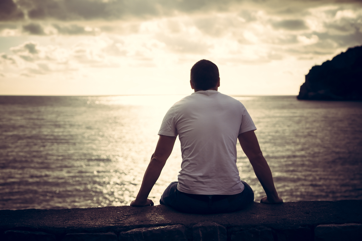 Lonely man looking with hope at horizon with sunlight during sunset with effect of light at the end of tunnel